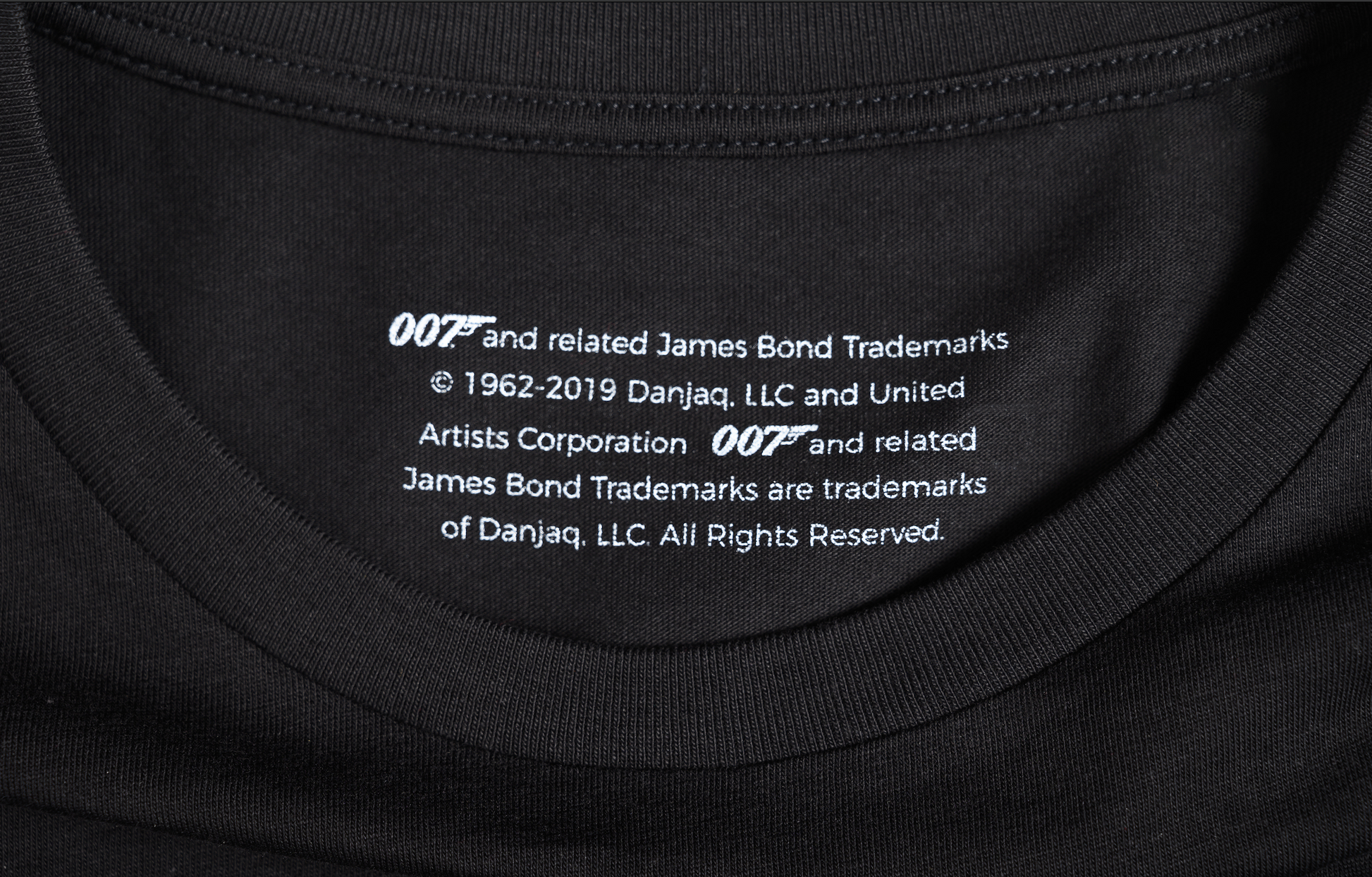 007 x SPYSCAPE T-Shirt - Close up of inside neck with size tag, "007 and related James Bond Trademarks, 1962-2019 Dan Janq, LLC and United Artist coorporation,  All rights reserved. 